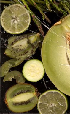 an assortment of fruits and vegetables cut in half on a black surface with green stems