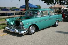 an old green car is parked on the side of the road next to other antique cars