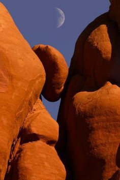 the moon shines brightly in the blue sky above some large rocks and rock formations