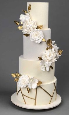 a three tiered cake with white flowers and gold leaves