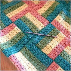 the crocheted blanket is laying on the table with a needle sticking out of it