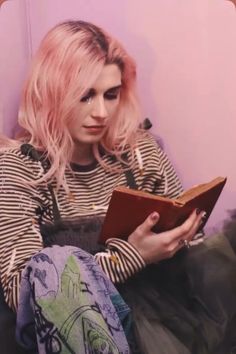 a woman with pink hair is sitting on the floor and holding a book in her hands