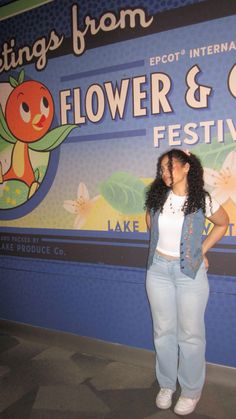 a woman standing in front of a flower and garden festival sign with her hands on her hips