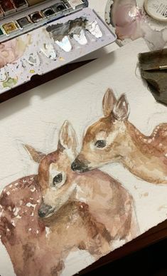 a painting of two fawns sitting on top of a table next to paintbrushes