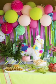 a table topped with lots of desserts and colorful paper pom poms hanging from the ceiling