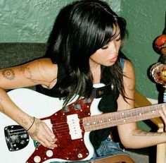 a woman sitting on a couch with a guitar in her hand and tattoos on her arm