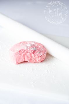 a pink doughnut sitting on top of a white tablecloth covered in powdered sugar