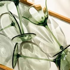 three green glasses sitting on top of a wooden tray next to each other in front of a white wall