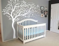 a baby's room with a white crib and tree decal on the wall