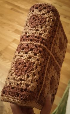 a person holding up a crocheted blanket on top of a hard wood floor