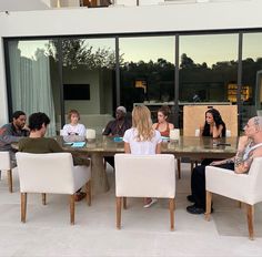 a group of people sitting around a wooden table in front of large windows with sliding glass doors