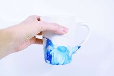 a hand holding a coffee mug with blue ice on the inside and white frosting on the outside