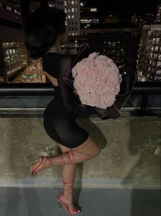 a woman holding a bouquet of roses on top of a building in the city at night