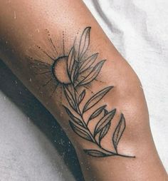 a close up of a person's leg with a tattoo on it that has leaves and a sun in the background