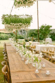 a long wooden table topped with vases filled with flowers next to tables covered in chairs