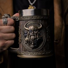 a person holding a large metal mug with an image of a horned man on it