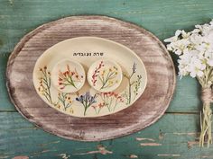 two plates with flowers painted on them are sitting on a wooden table next to some dried flowers