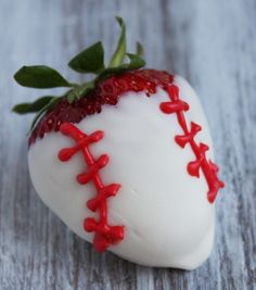 a white chocolate covered strawberry with red stitches and a green sprig on top