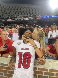 two women kissing each other in front of a crowd at a football game with fans