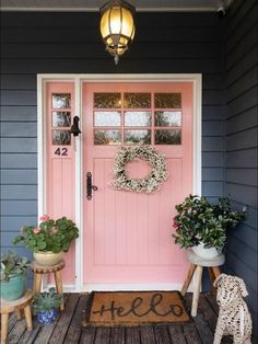 a pink front door with two potted plants next to it and a welcome mat