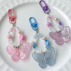 three butterfly shaped key chains on a white plate with beads and clips attached to them