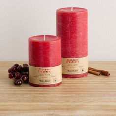 two red candles sitting on top of a wooden table next to cinnamon sticks and berries