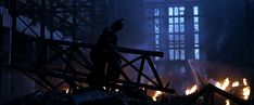 a man standing on top of a wooden structure in the middle of a building filled with fire