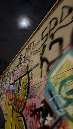 a man standing next to a wall covered in graffitti under a full moon