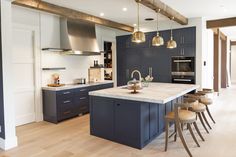 a large kitchen with blue cabinets and wooden flooring is pictured in this image, there are several stools around the island