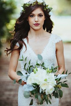 a woman in a wedding dress holding a bouquet of flowers and greenery on her head