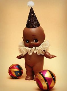 an adorable little baby doll with a party hat on and some balls in front of it