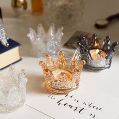 three glass crowns sitting on top of a white table next to books and candle holders