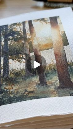 an open book with watercolors on it and a painting of trees in the background