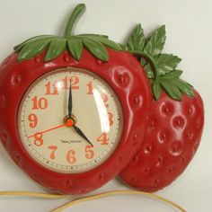 a red clock with two strawberries attached to it's sides on a white wall