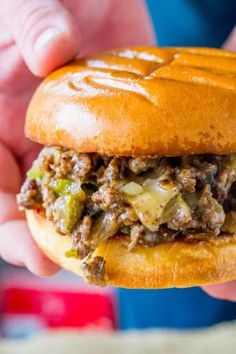 a close up of a person holding a sandwich in their hand with meat and vegetables on it