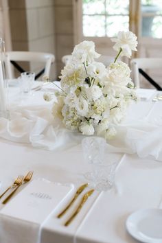 a table with white flowers and gold place settings