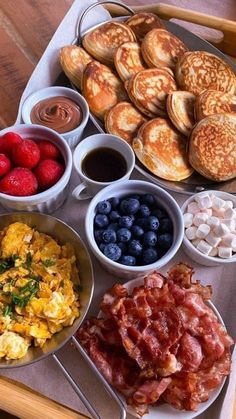 a breakfast tray with pancakes, eggs, berries and other foods in bowls on it