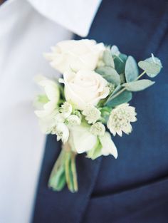 a boutonniere with white flowers and greenery on it's lapel