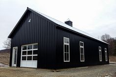 a black barn with two windows and a white door on the front is shown in an empty lot