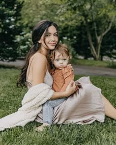 a woman sitting in the grass holding a baby