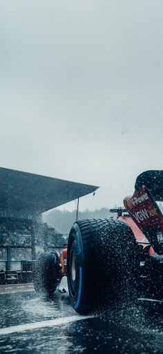 a red and white race car driving through the rain with it's front wheels out