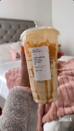 a person holding up a cup with caramel sauce on it in front of a bed