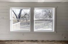 an empty room with two windows in the middle and wood flooring on the other side