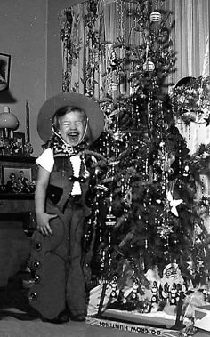 an old photo of a child standing in front of a christmas tree with decorations on it