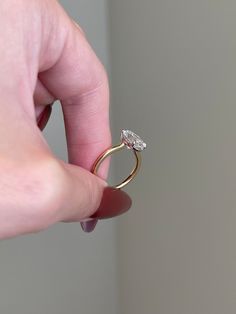 a hand holding a ring with a diamond on it's middle finger, in front of a white wall