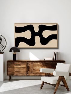 an abstract painting hangs on the wall next to a white chair and sideboard with a lamp