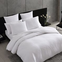 a bed with white sheets and pillows in a room next to a black chair on the floor