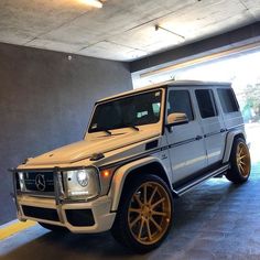 a white mercedes g - class parked in a parking garage with yellow rims and gold wheels