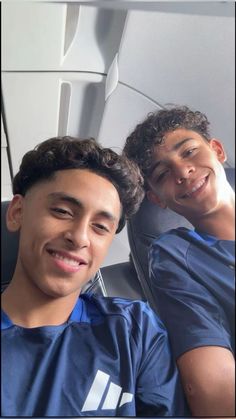 two young men sitting next to each other in an airplane seat smiling at the camera