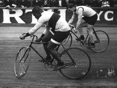 two men riding bikes on a wooden floor in front of a crowd with people watching